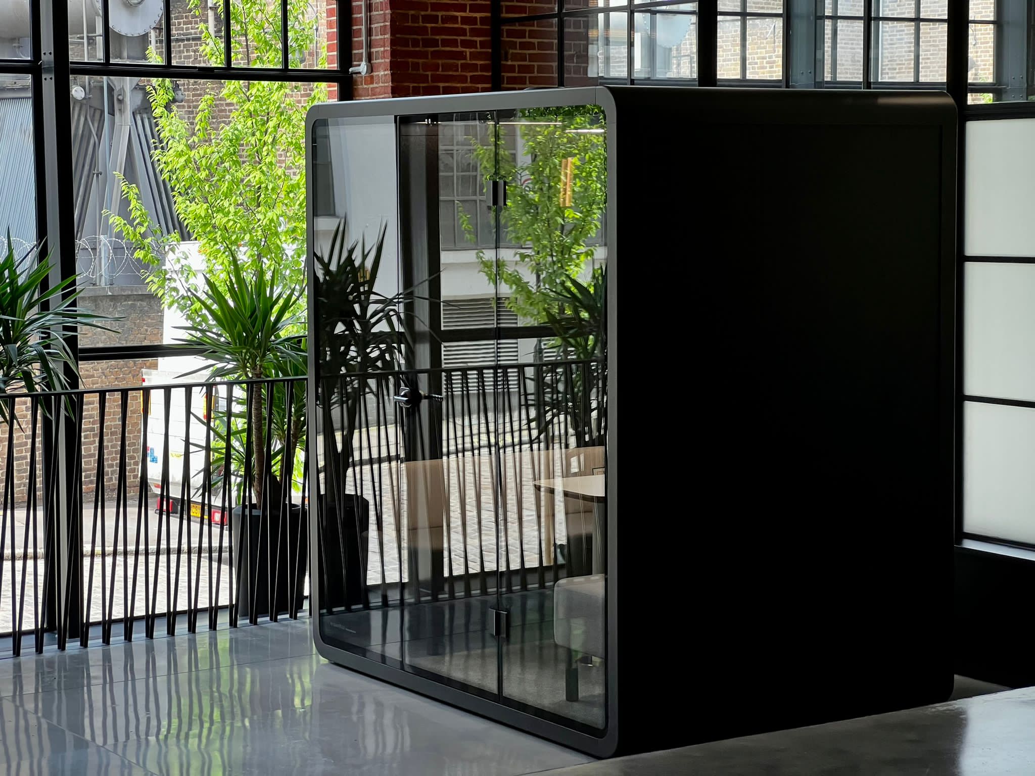 Cabine acoustique  pour quatre personnes avec parois vitrées, deux canapés et table centrale, bureau moderne